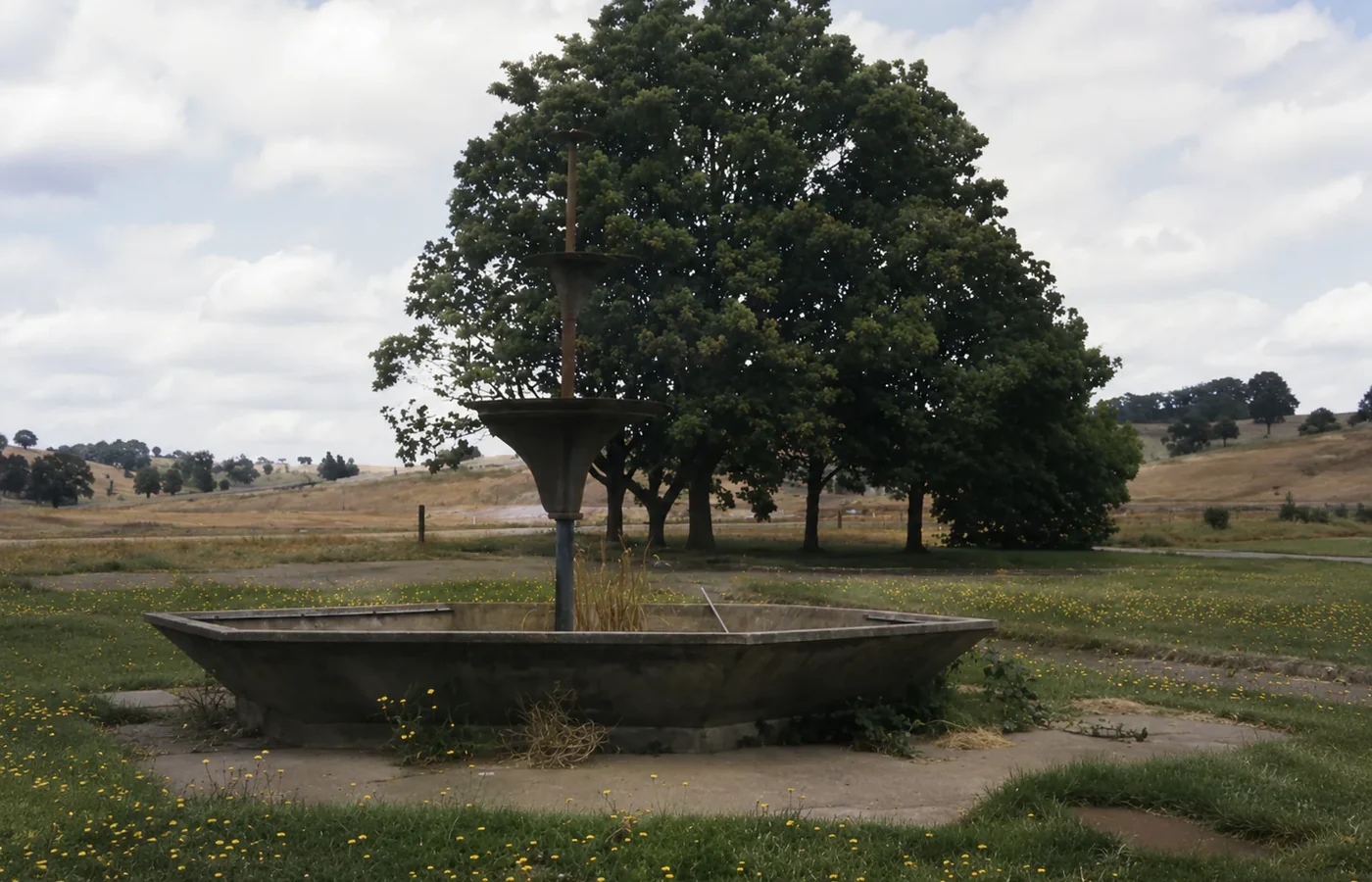 The disused Monash Square fountain standing in open ground after Yallourn's removal, with established trees behind it.