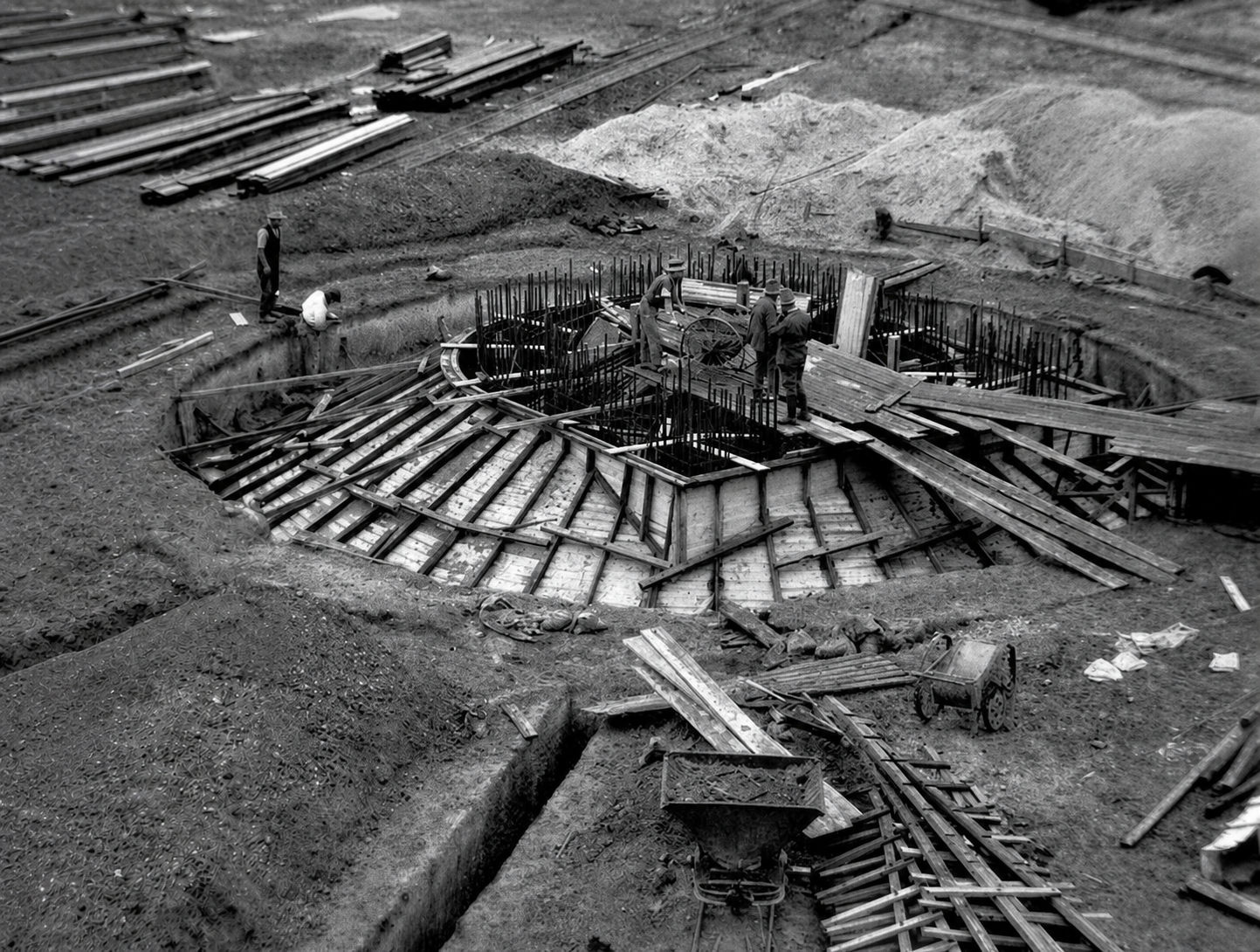 Reconstructed black-and-white historical photograph showing workers, timber formwork and dense reinforcing steel in the circular foundation of the Yallourn briquette-works chimney.