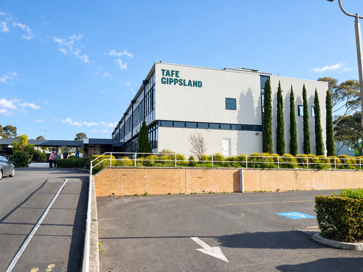 Enhanced daylight view of a TAFE Gippsland building at the Yallourn campus, with ramps, parking and the institution’s name on the facade.