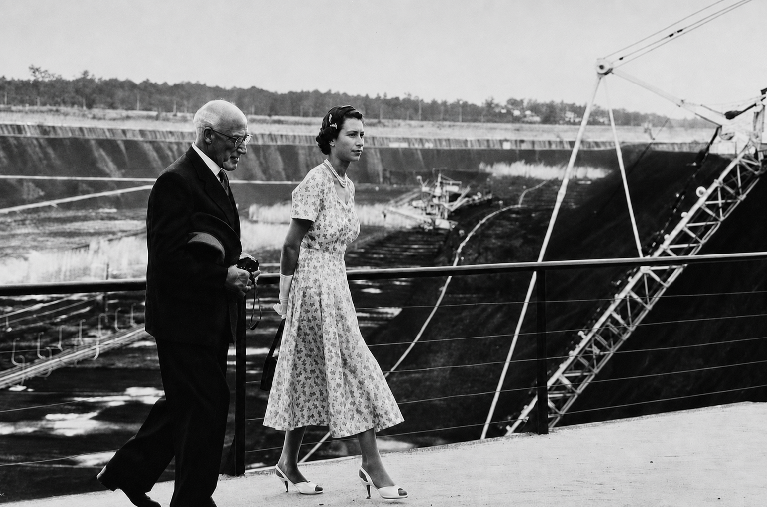 Queen Elizabeth II and an accompanying official walk along a railing above the terraced Yallourn open-cut mine.