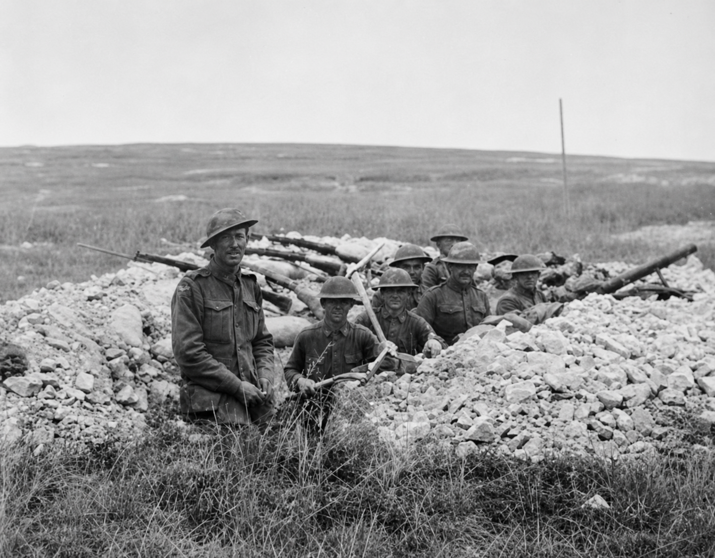 Australian and American soldiers stand and sit together in a shallow trench at Hamel.
