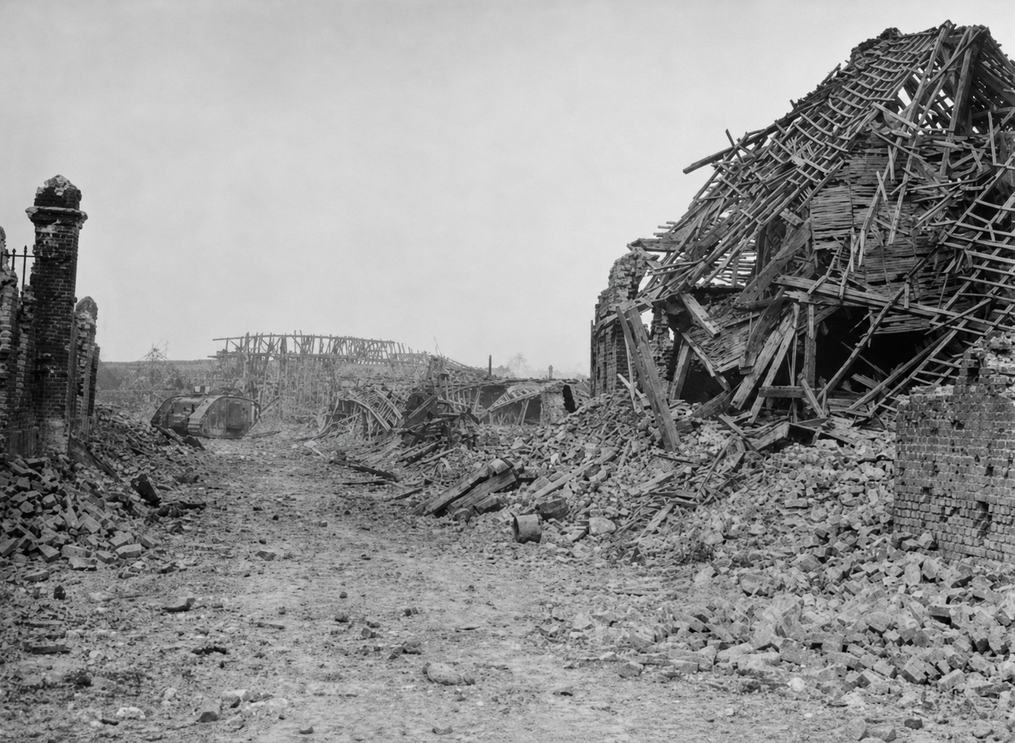 A ruined street in Hamel with collapsed buildings and a disabled tank in the distance.
