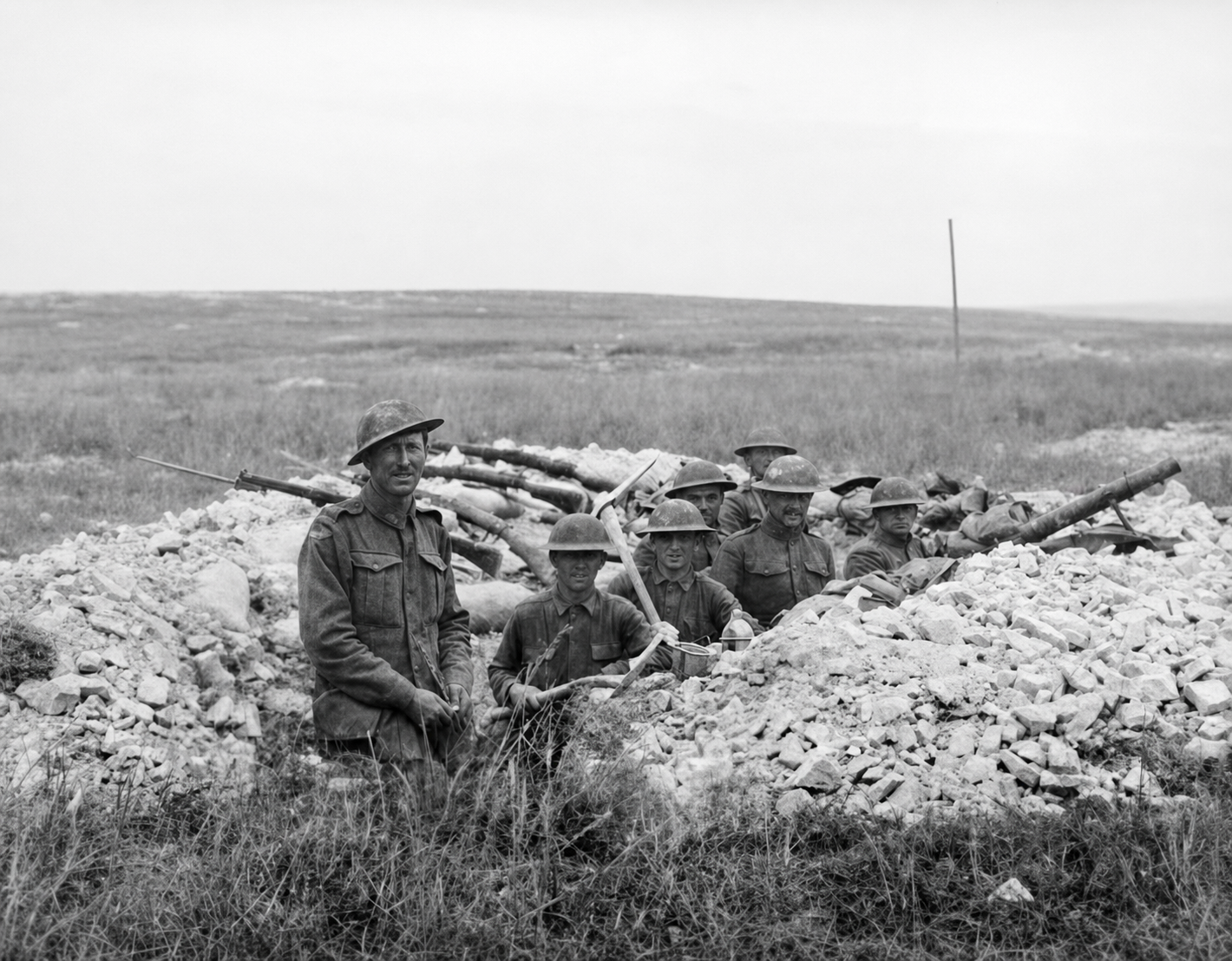 Australian and American soldiers stand and sit together in a shallow trench, with open ground behind them.