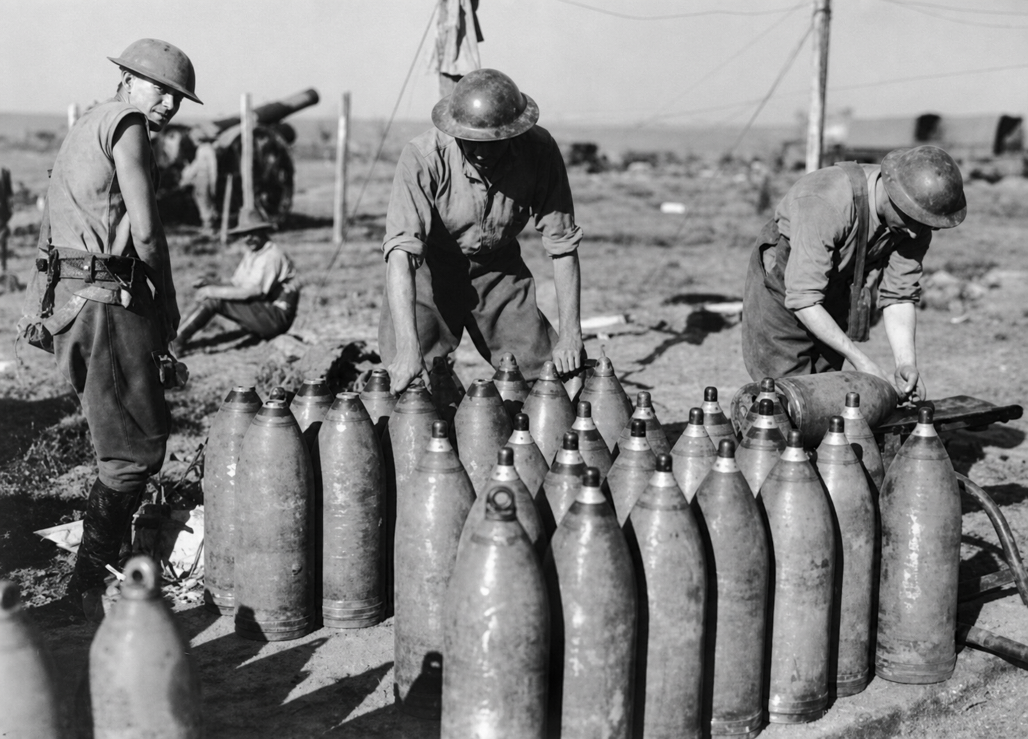 Artillerymen work beside rows of large shells, tools and timber supports.
