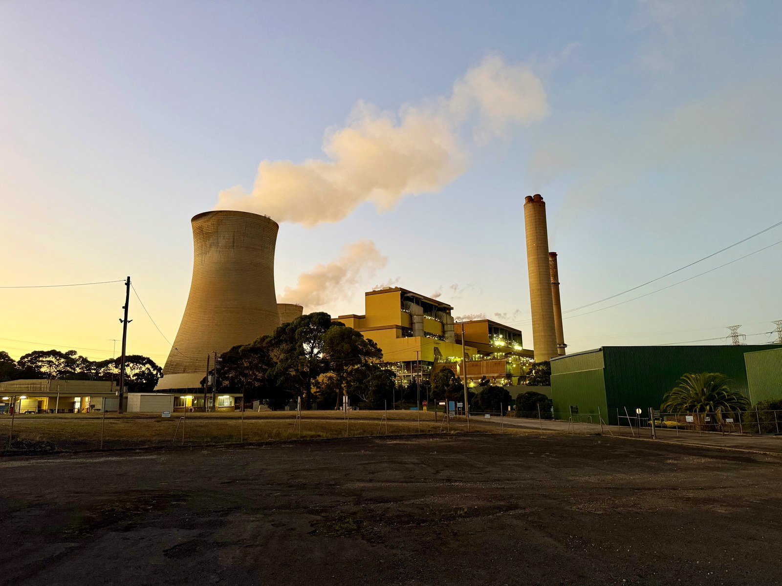 Yallourn W at dusk, showing a cooling tower, tall chimneys and illuminated station buildings beneath a pale sky.