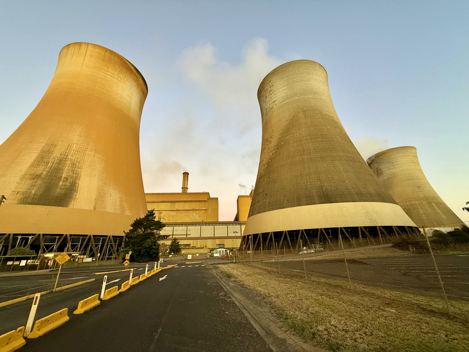 Low-angle view of three massive curved concrete cooling towers beside Yallourn W station buildings.