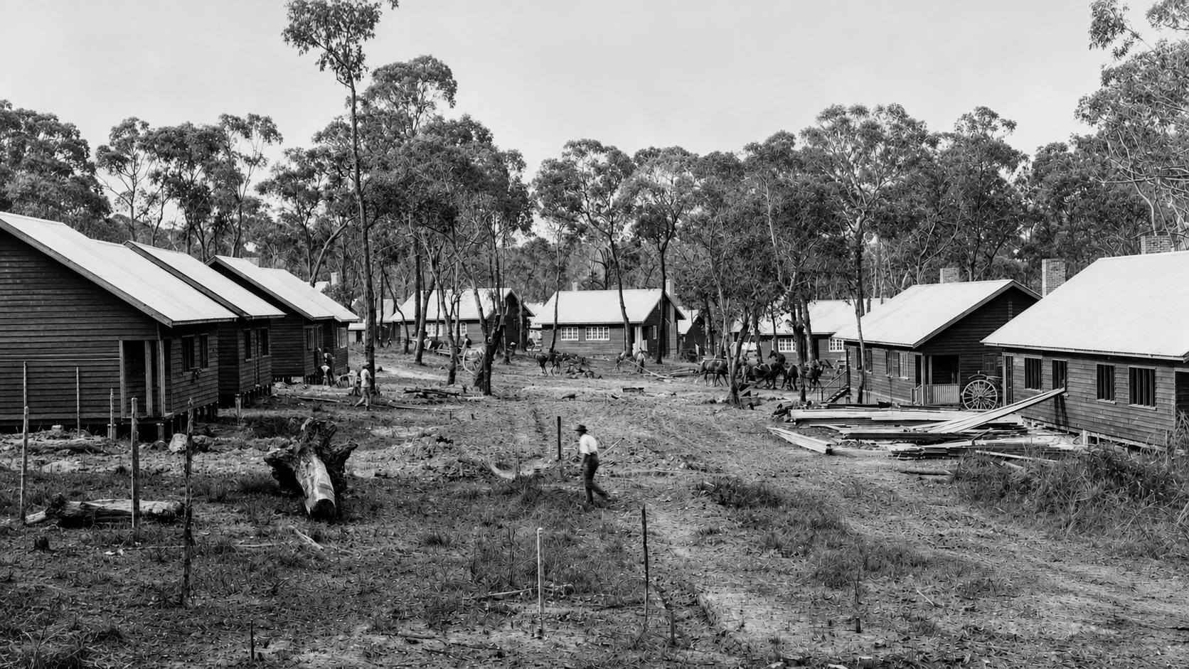 Timber houses stand among cleared ground and remaining trees at early Yallourn, with people and building materials visible along the unmade street.