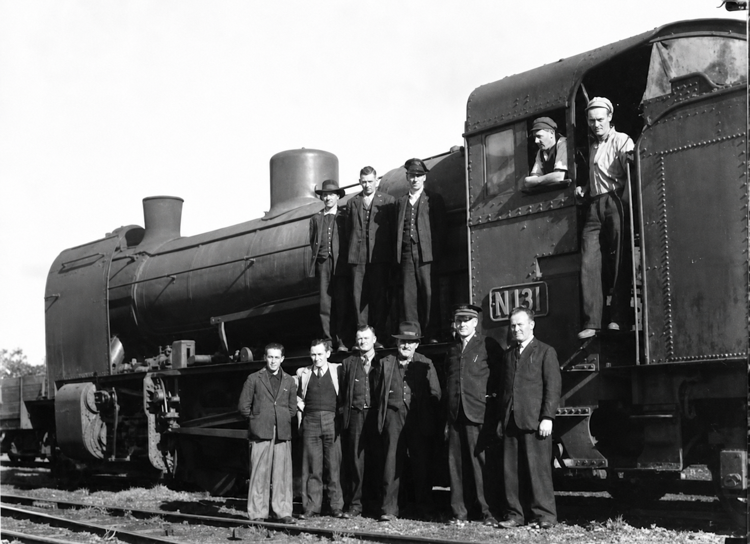 A group of railway employees pose beside and on steam locomotive N 131, with several men standing at track level and others on the engine and cab.