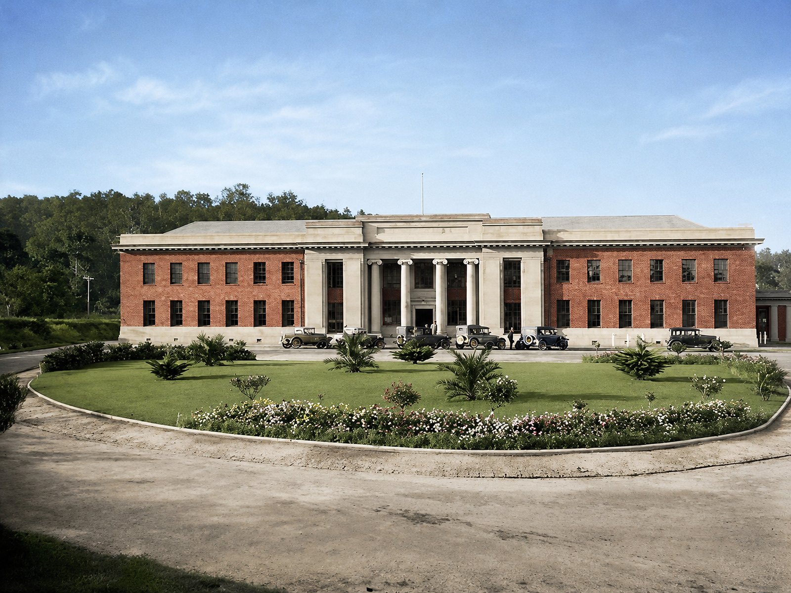 Colourised historical view of the Yallourn Production Centre with a circular garden and early cars at the entrance.