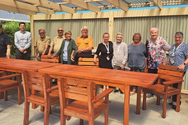 Members standing behind completed wooden furniture