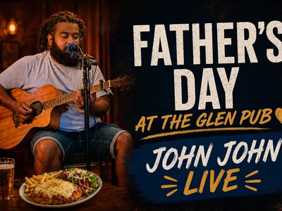 A live musician playing acoustic guitar on a pub stage decorated for Father's Day, with a chicken parma and cold drink on a nearby table.