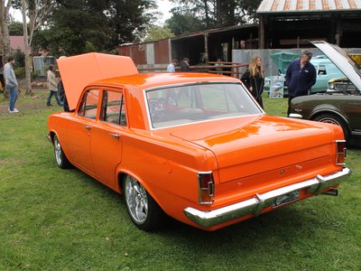 A row of polished classic cars and motorcycles displayed on grass at Old Gippstown in Moe on a sunny morning.