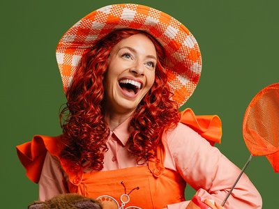 A performer dressed as Emma Memma on a colourful stage set with children in the audience dancing and clapping along.