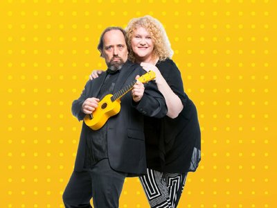 Two cabaret performers on a theatrical stage, dressed in colourful sixties-inspired costumes, mid-performance with expressive gestures.