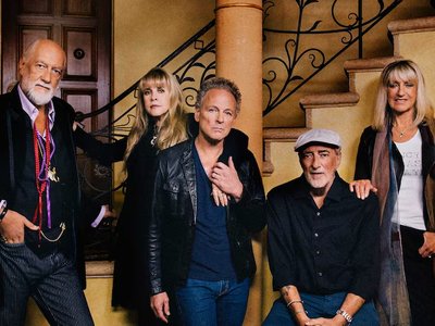 A band performing on a lit stage in a performing arts venue, evoking the classic rock sound and era of Fleetwood Mac.