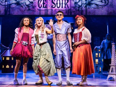 A vibrant stage production still showing performers in colourful costumes mid-song, capturing the energy of a pop jukebox musical.
