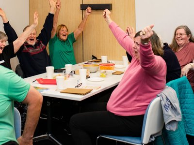 Groups of adults seated around tables at a library event, engaged in a trivia night with answer sheets and refreshments.
