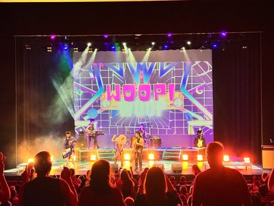 A lively 80s-themed fundraiser event with guests in colourful retro costumes dancing under disco lights in a Gippsland venue.