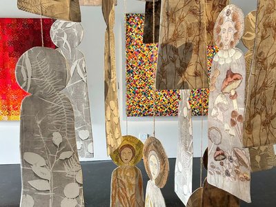 A close-up of layered textile artworks featuring intricate stitching, soft sculpture, and repurposed fabric in warm and earthy tones displayed in a gallery setting.