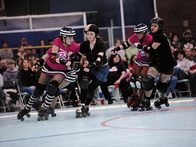Young girls in roller skates and protective gear practising skating moves on an indoor rink.