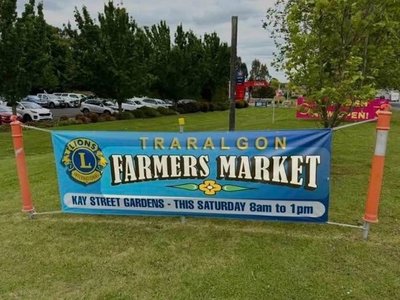 A bustling outdoor farmers market with colourful stalls of fresh fruit, vegetables and handmade products set among gardens.