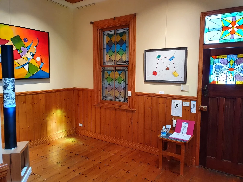 A timber-panelled room inside Matchbox Gallery with leadlight panels in a window and front door and framed artworks on the walls.