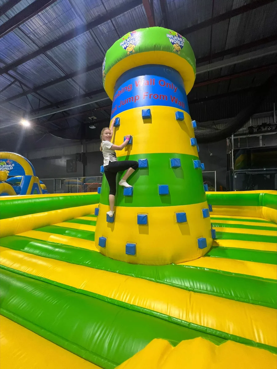 A child climbing a tall green and yellow inflatable wall inside Stadium 34.