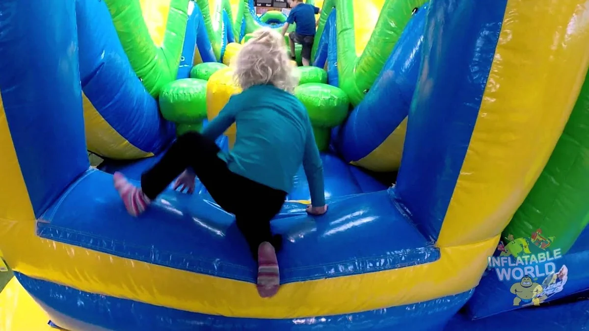 A child crawling through a blue, green and yellow Inflatable World obstacle course.