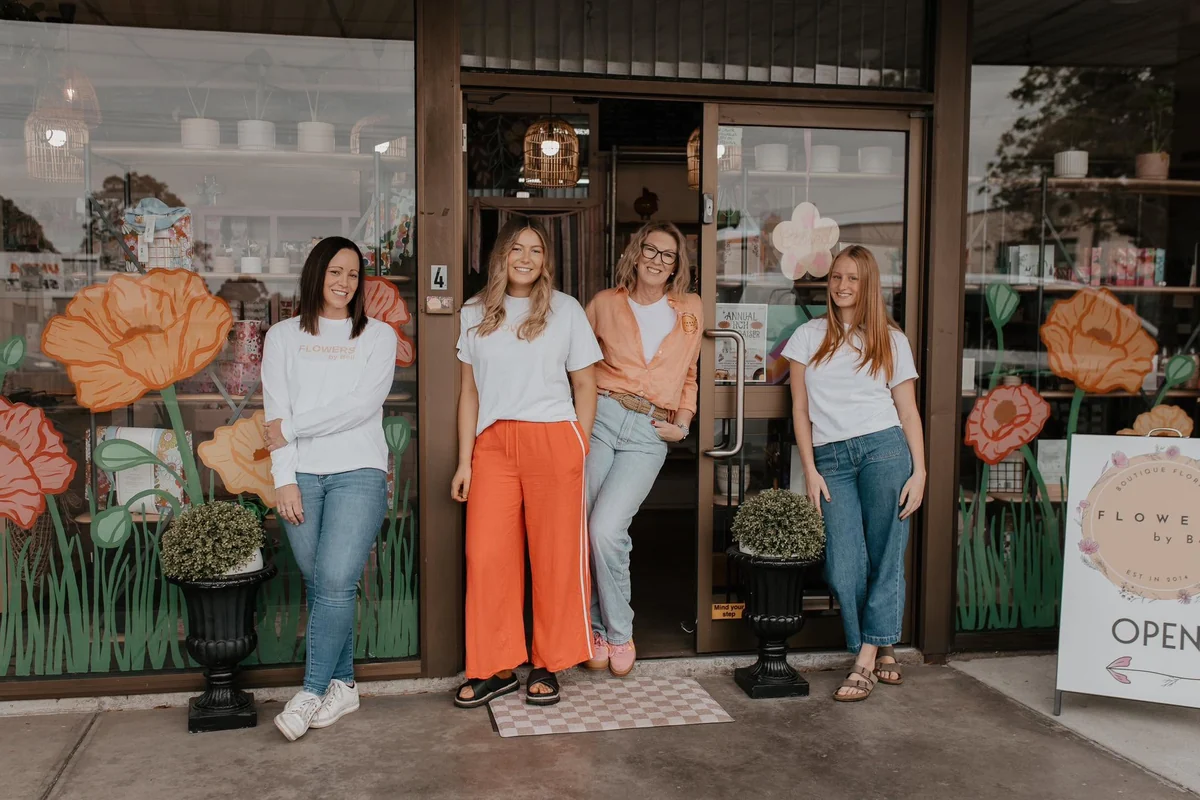 Four Flowers by Bell team members stand outside the Traralgon shopfront, framed by large orange flowers painted across the windows.