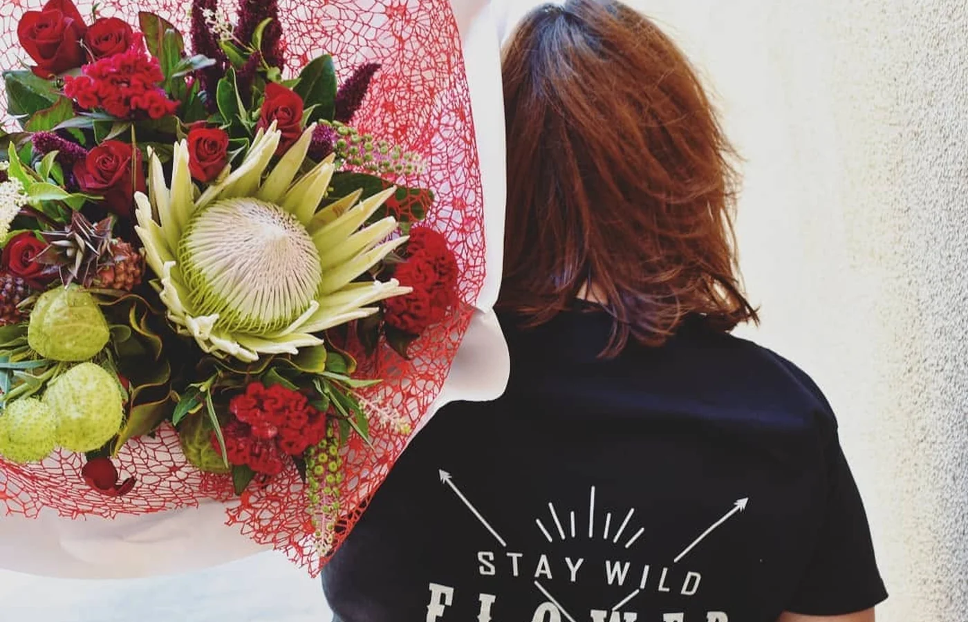 A florist seen from behind carries a large arrangement of red flowers and native foliage.