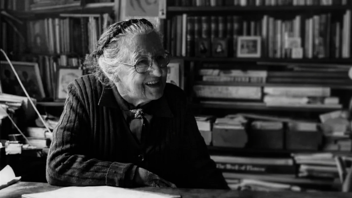 Jean Galbraith smiling while seated in front of shelves filled with books.