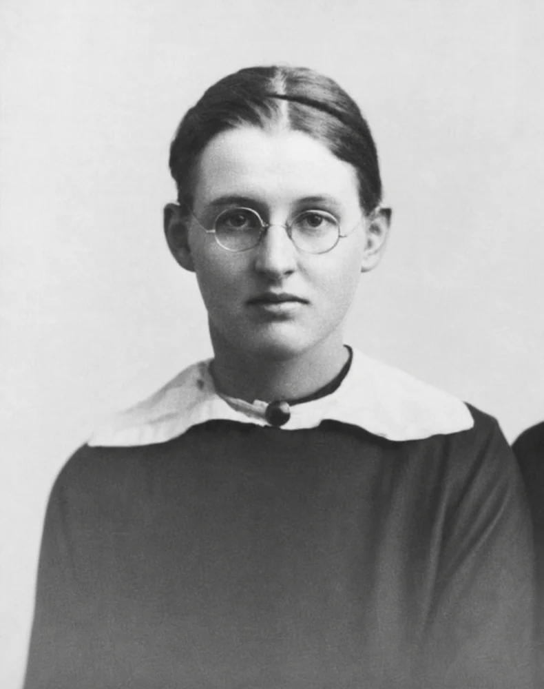A black-and-white portrait of young Jean Galbraith in the early 1920s, wearing round glasses and a white-collared top.