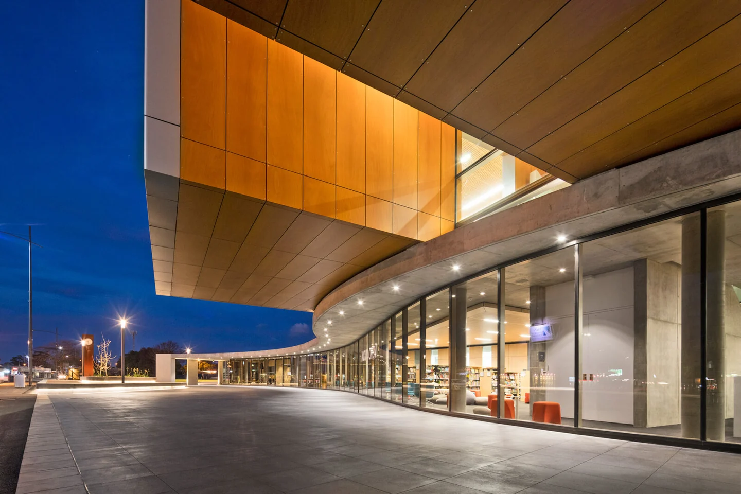 The curved glass frontage of the Frank Bartlett Memorial Library and Moe Service Centre illuminated at dusk.