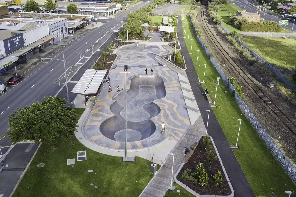 People gather beneath the angular shelter beside Moe Skatepark and the railway precinct.