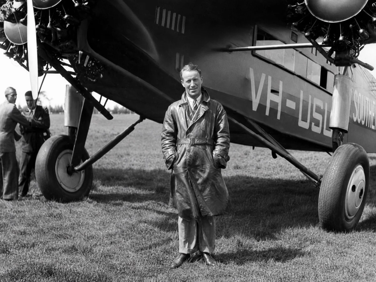 Restored black-and-white photograph of Sir Charles Kingsford Smith standing beside the Southern Cross aircraft at Morwell in 1932.
