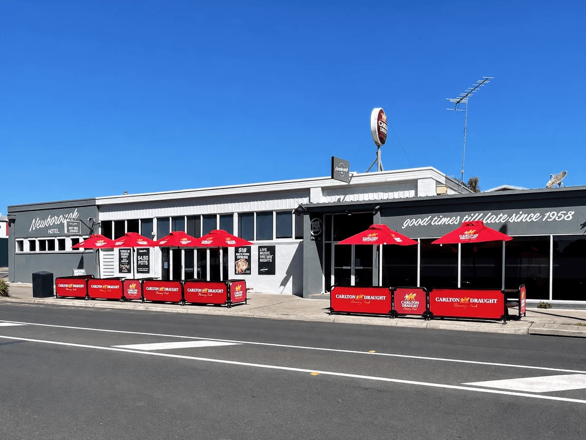 Newborough Hotel exterior in bright sunlight with red umbrellas along the footpath.