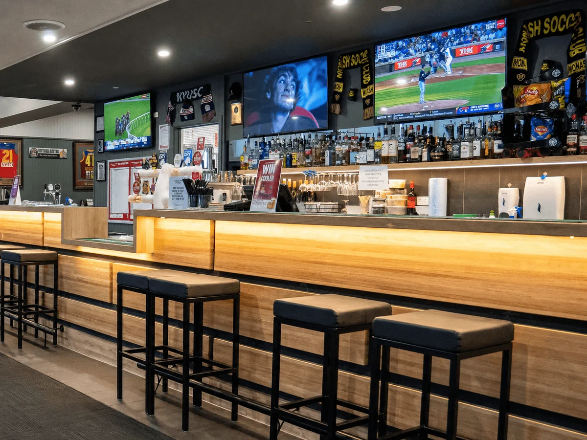 Timber-fronted bar with stools and sports screens inside Newborough Hotel.