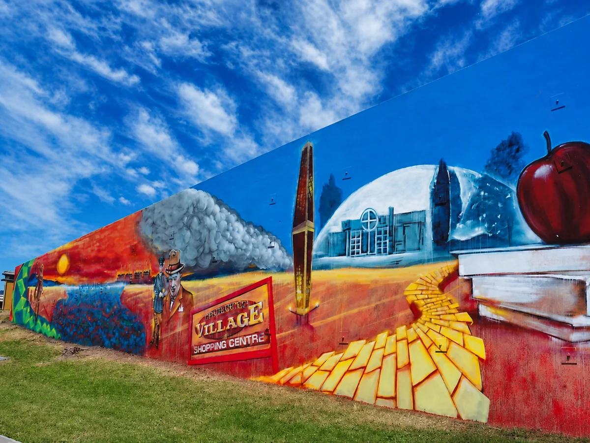 A long Churchill history mural showing the town symbol, a church, an apple and scenes of local industry beneath a vivid blue sky.