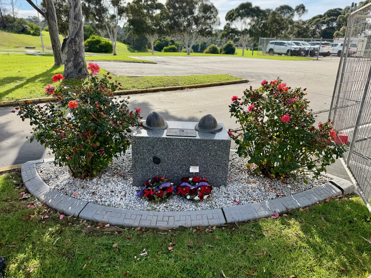 A granite service memorial with two sculpted military helmets, wreaths and red rose bushes.