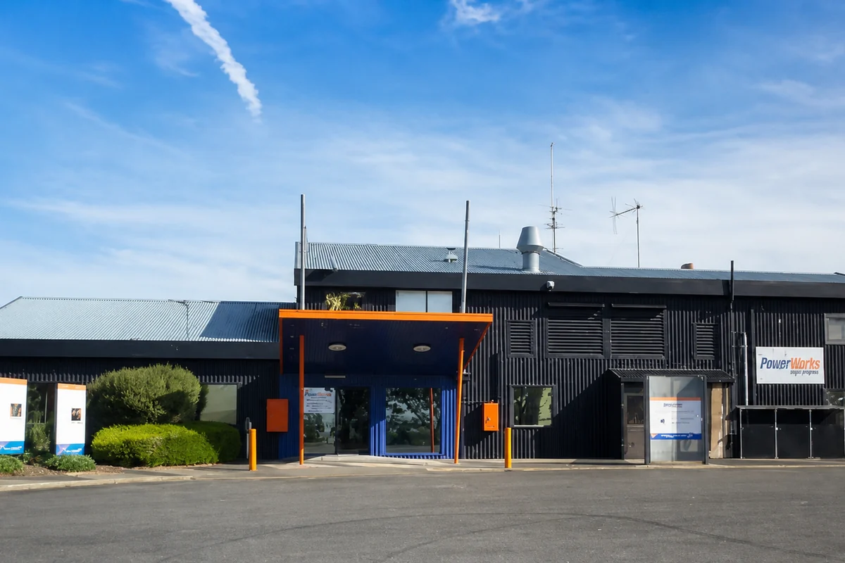 The dark-clad PowerWorks building with its orange entrance canopy and signs visible from the car park.