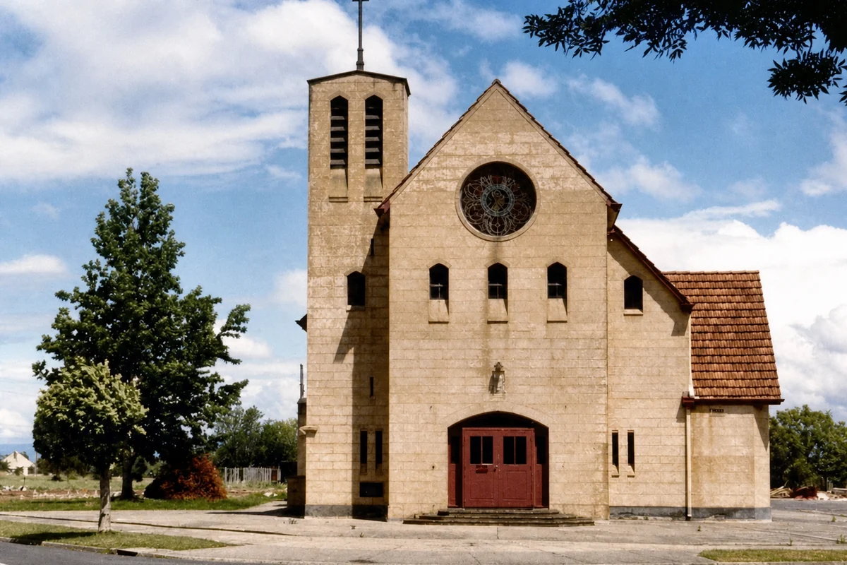 A stone church in Yallourn with a bell tower, cross, rose window and red doors.