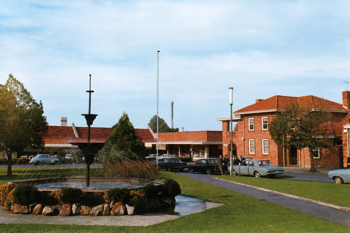 Yallourn's fountain in a landscaped civic square, with tiled-roof buildings and period cars beyond.
