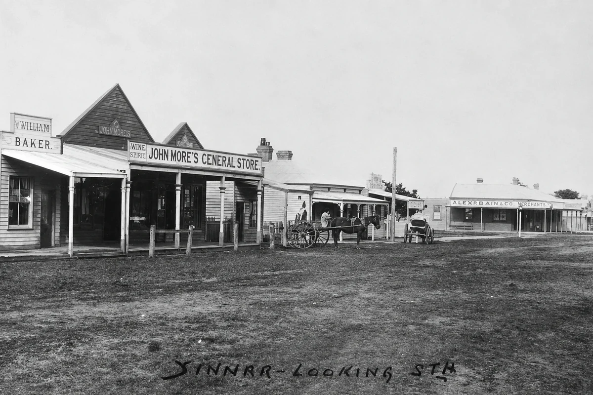 An early-1900s monochrome view along Yinnar's unsealed Main Street with timber shopfronts, horses and wheeled vehicles.