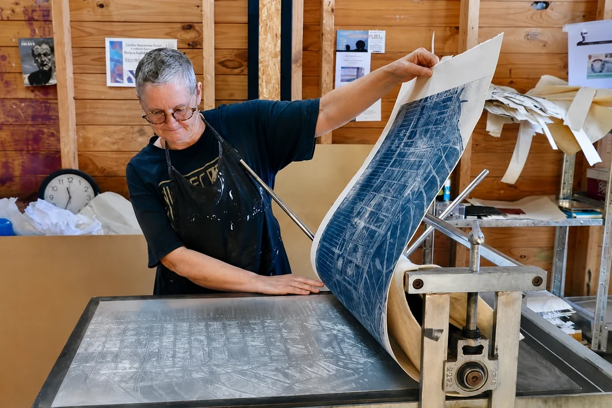 A printmaker lifts a large blue print from a press inside ARC Yinnar's timber-lined printmaking studio.