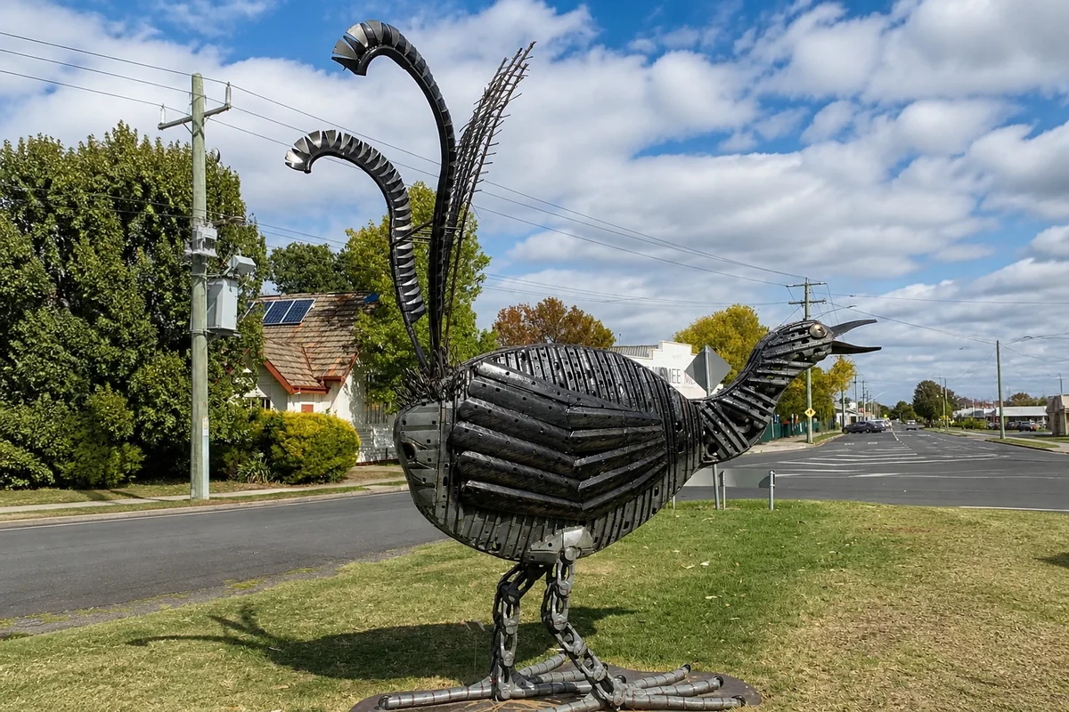 A large bird sculpture assembled from shaped metal components stands beside a Yinnar street.