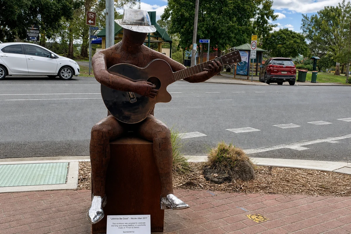 The seated metal sculpture Johnnie Be Good holds a guitar beside Yinnar's Main Street.