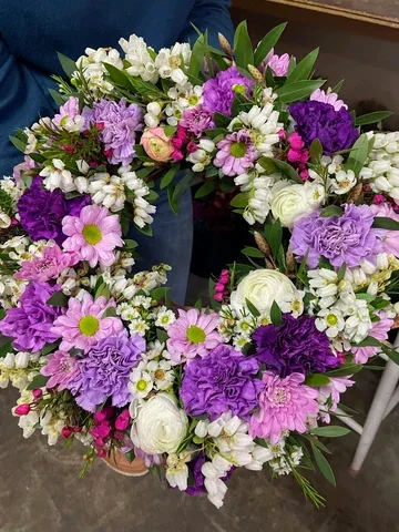A circular wreath of purple, pink and white flowers with green foliage.