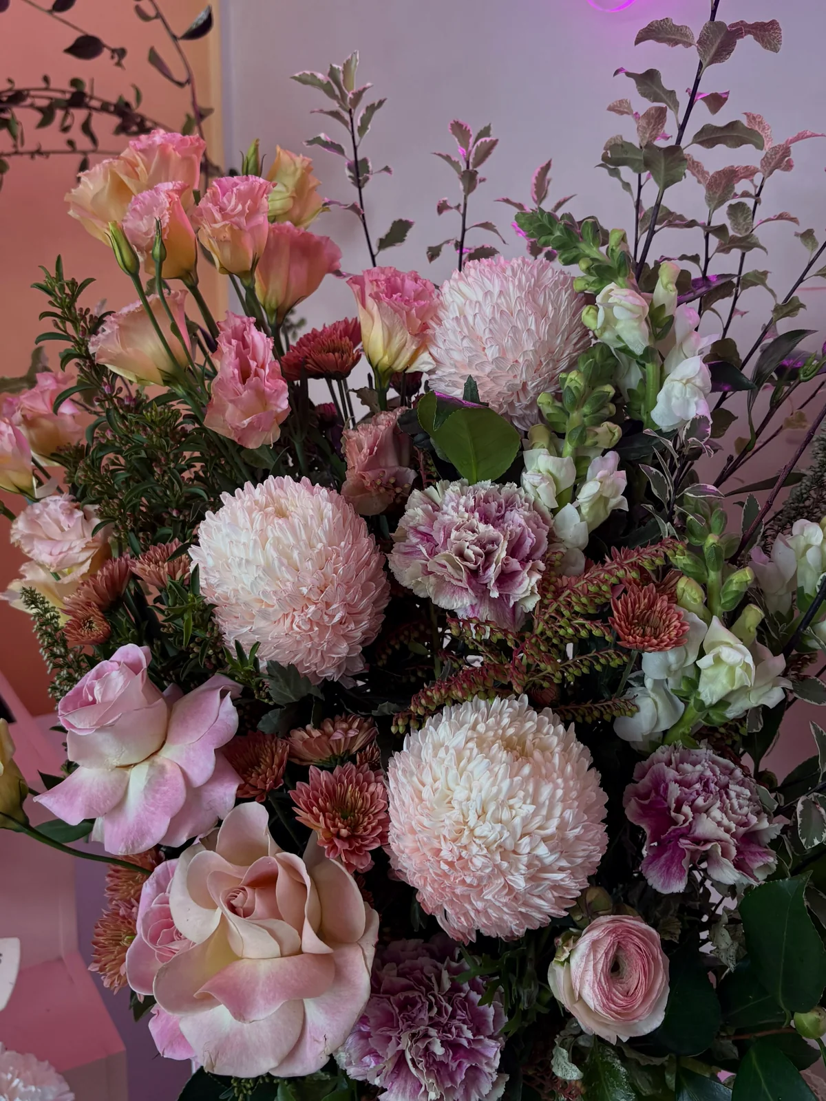 Pink, peach and cream flowers arranged beneath soft pink shop lighting.