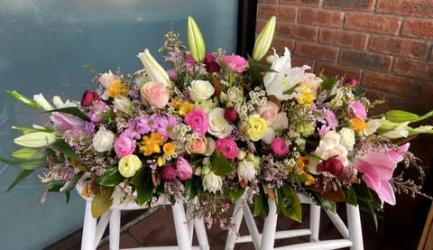 A wide pastel funeral flower arrangement displayed on a white stand.