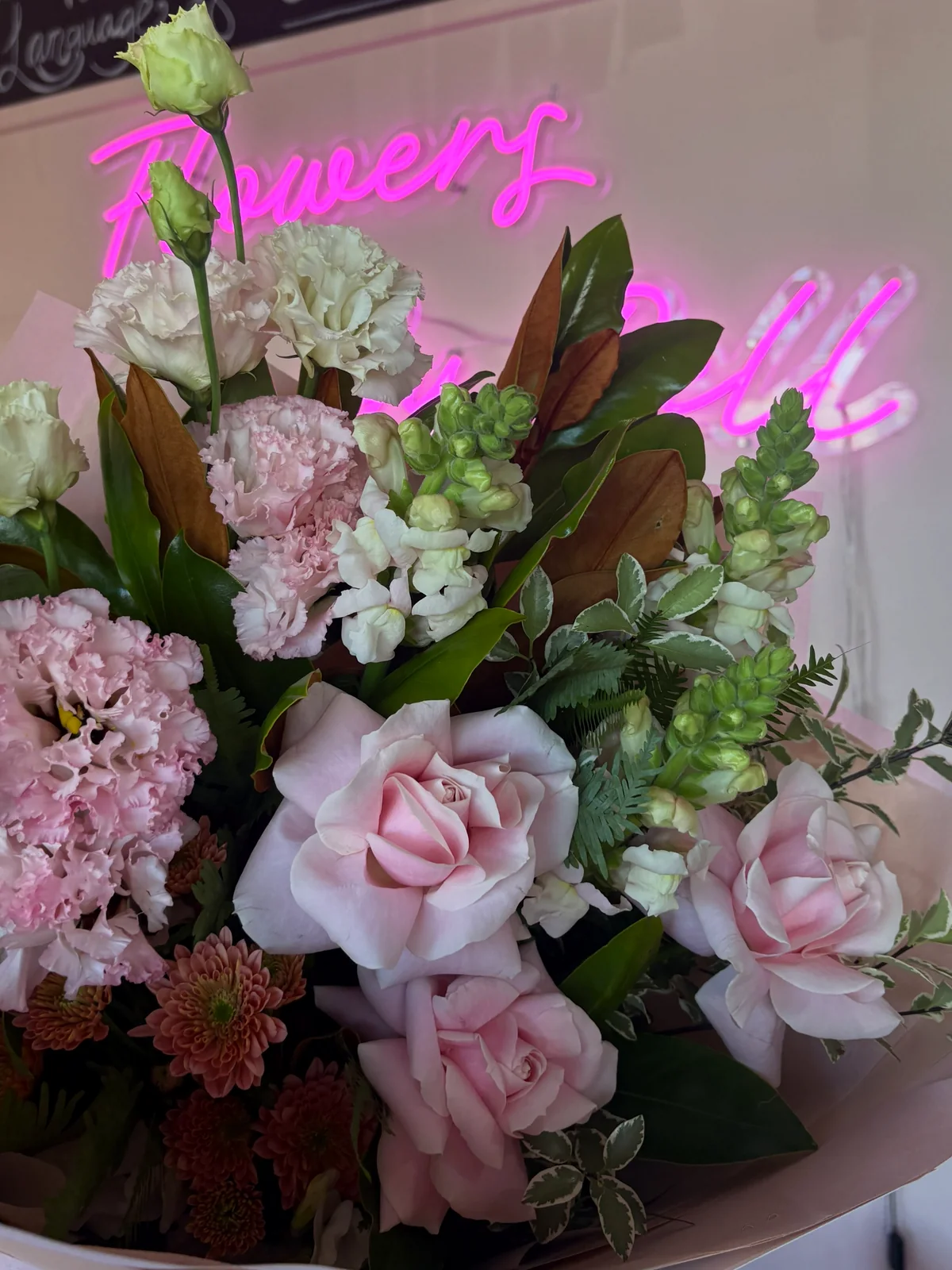 Pink and white flowers arranged in front of a pink neon shop sign.